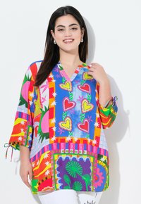 Tunique multicolore avec décolleté en V, manches mi-longues, ornée de motifs en forme de cœur, d'étoiles et d'un mélange de formes et de couleurs vibrantes.