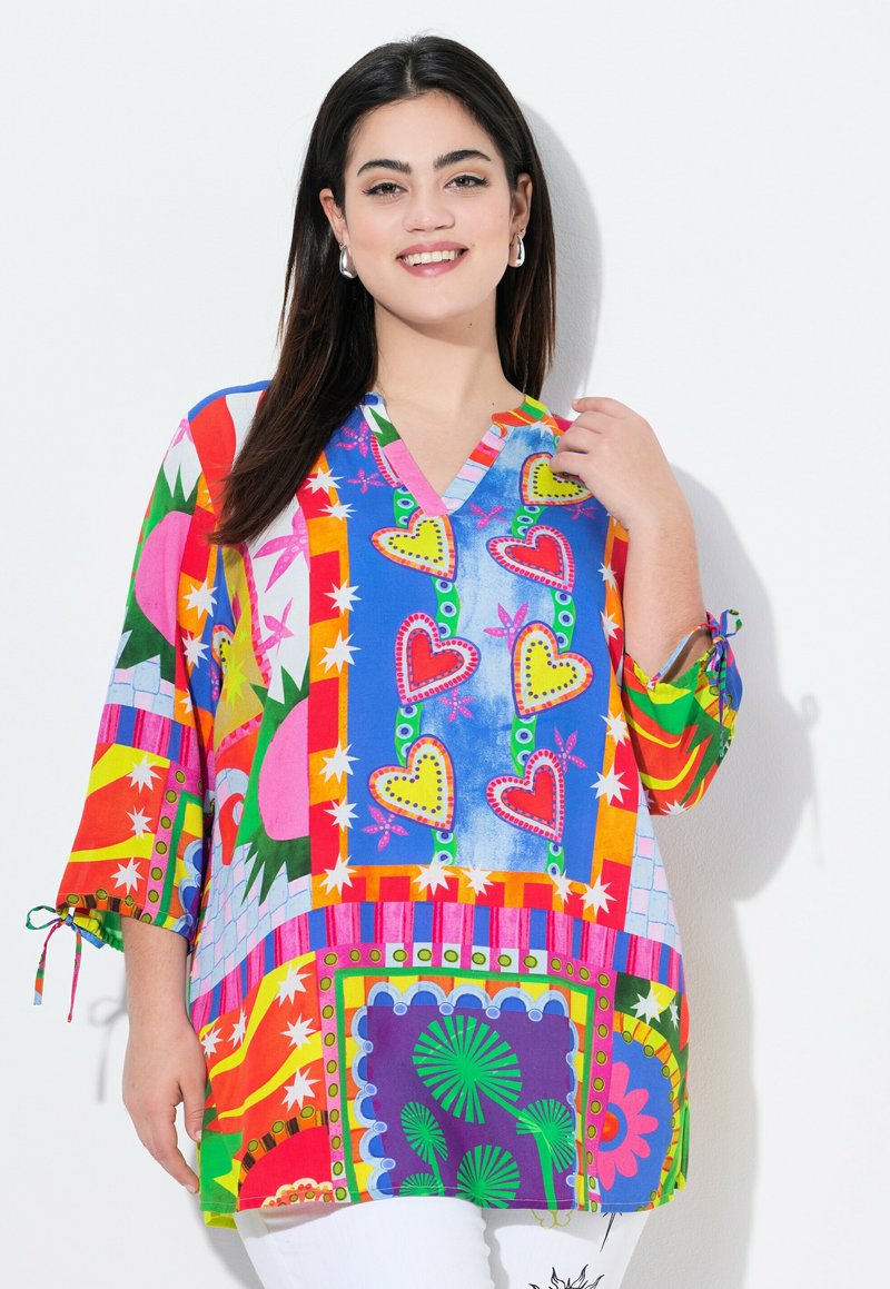 Tunique multicolore avec décolleté en V, manches mi-longues, ornée de motifs en forme de cœur, d'étoiles et d'un mélange de formes et de couleurs vibrantes.