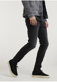 Czarne dżinsy z wąskim krojem, zestawione z czarnymi zamszowymi trampkami z kremową podeszwą. Całość uzupełnia wyblakła kurtka dżinsowa.