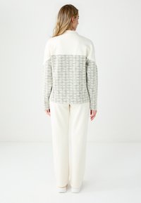 Veste légère avec un devant en nylon crème et un dos en tricot beige texturé. Comprend un col montant, des manches longues et une coupe décontractée.