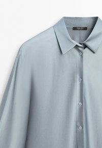 Camicia di raso azzurro chiaro con bottoni, colletto appuntito, bottoni visibili ed etichetta con la scritta Massimo Dutti made in China.