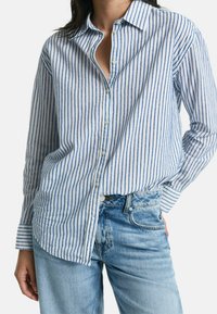 Blauw-witte gestreepte overhemden met kraag, lange mouwen en een relaxte pasvorm, gecombineerd met lichte spijkerbroek.