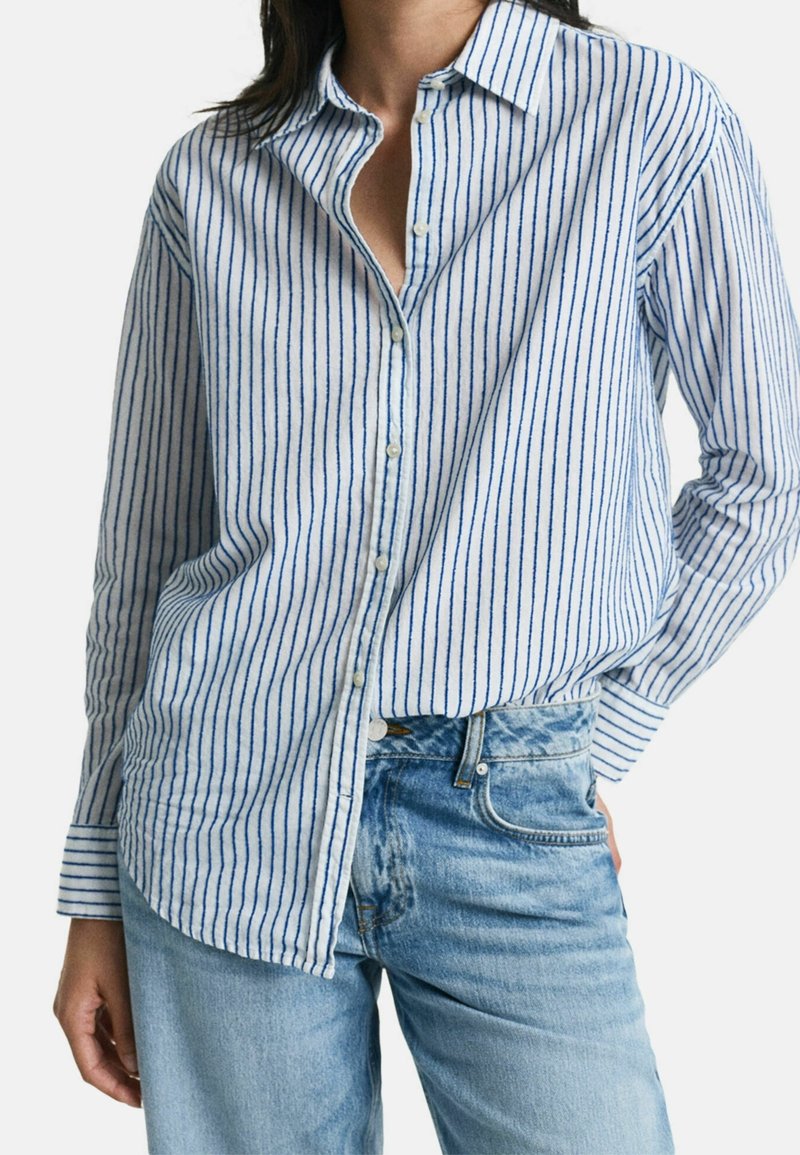 Blauw-witte gestreepte overhemden met kraag, lange mouwen en een relaxte pasvorm, gecombineerd met lichte spijkerbroek.