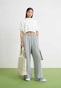 Sweatshirt branco cropped com bordado "NIKE 1972", combinado com calças de fato de treino cinza claro de perna larga com bolsos cargo, e uma mala tote matelassê bege.