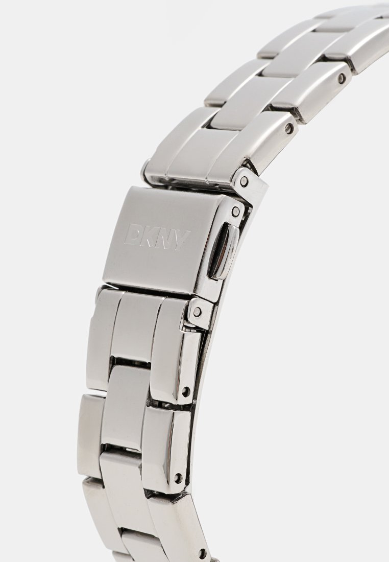 Bracelet de montre en acier inoxydable argenté avec une finition polie, featuring des maillons entrelacés et un logo DKNY sur le fermoir.