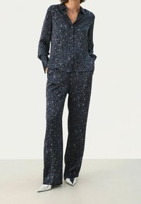 Navy satijnen pyjama set met een luipaardprint. Lange mouwen overhemd met knopen, gecombineerd met bijpassende wijde broek. Zilveren schoenen.