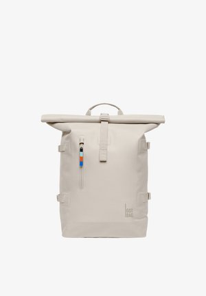 Sac à dos beige à rabat roulé avec poche zippée verticale à l'avant, tirette de fermeture éclair bicolore, sangles de compression latérales, et logo "GOT BAG" en bas à droite.