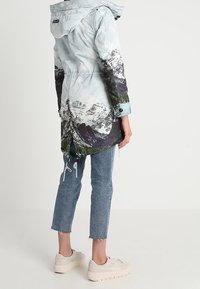 Vaaleansininen parkatakki, jossa vuorikuvio, huppu ja kiristys vyötäröllä. Yhdistetty kuluneisiin farkkuihin ja vaaleanriaisiin lenkkareihin. Rentoa ulkoilutyyliä.