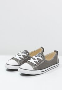 Sneaker in tela grigia con punta in gomma bianca, lacci bianchi e dettagli neri sulla suola e sul tallone. Design semplice con una silhouette a bassa angolazione.