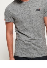 Grå t-shirt med kort ärm gjord av ett texturerat tyg, med en liten logotyp i mörkblått på bröstet och en orange detalj på ärmen.