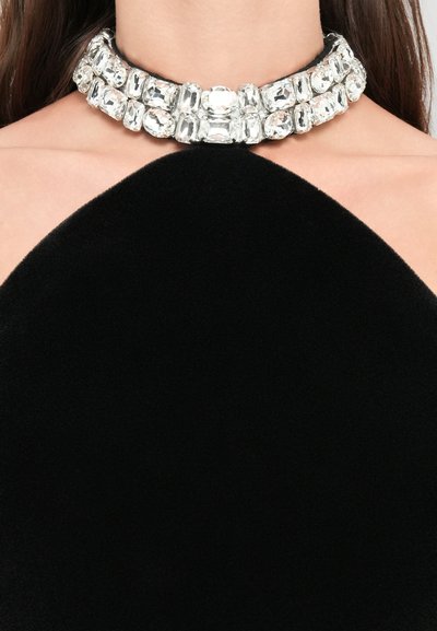 Der Hals ist mit einer doppelten Reihe großer, rechteckiger, klarer Edelsteine geschmückt, die als Choker über einem schwarzen hochgeschlossenen Kleidungsstück getragen werden.