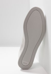 Bílé tenisky s texturovanou šedou gumovou podrážkou, s hladkým svrškem a akcenty z semiše. Značka viditelná na podrážce.