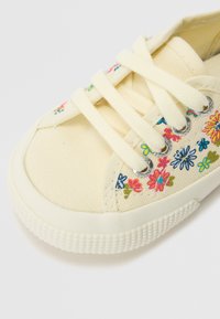 Gul kanvas sneakers med blomsterbroderi i rosa, blått og grønt. Har rund tå, gummisåle og flate snørebånd.