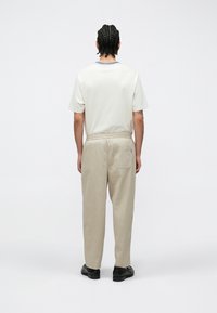 T-shirt en coton beige clair avec un design simple, associé à un pantalon beige clair avec une taille élastique et une poche arrière. Chaussures noires.