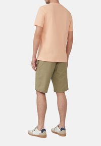 Perzikkleurig t-shirt met korte mouwen, gecombineerd met olijfgroene shorts. Het model draagt witte sneakers met marineblauwe accenten. Eenvoudige, casual outfit van achteren.