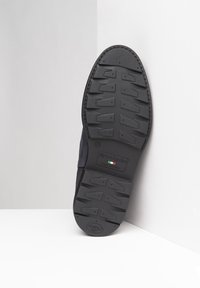 Semelle en caoutchouc noir avec des motifs profonds, arborant un logo. Tige en daim bleu marine, avec des détails cousus le long du bord. Fabriqué en Italie.