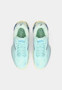 Sapatos de desporto azul claro com parte superior em malha, sola espessa e acentos amarelos. As características incluem fecho com atacadores e detalhes com logótipos.