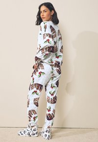 Fleece pyjama set met een witte achtergrond en een print van luipaard en hulst. Inclusief bijpassende instapslippers met een soortgelijk ontwerp.