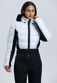 Weiß schwarze Steppjacke mit hohem Kragen, Reißverschluss, abnehmbarem Pelzbesatz und tailliertem Schnitt. Mit seitlichen Reißverschlusstaschen.