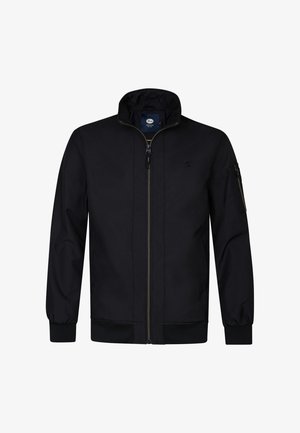 Czarna kurtka bombowiec z wysokim kołnierzem, przednim zamkiem błyskawicznym i ściągaczami na mankietach. Ma kieszeń na zamek błyskawiczny na lewym rękawie. Gładka struktura.