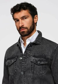 Giubbotto in denim nero con collo, due tasche frontali e dettagli con bottoni in argento. Presenta un tessuto testurizzato e cuciture visibili.