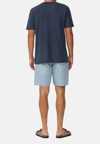 Navy-blaues T-Shirt mit kurzen Ärmeln aus Baumwolle, lässiges Design, kombiniert mit hellblauen Denim-Shorts und braunen Sandalen.