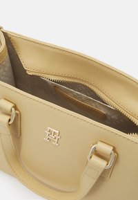 Gul lærveske med gullfarget hardware, med en glidelåslomme og mønstret interiørfôr. Kompakt design med robuste håndtak.