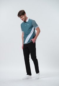 Teal polo-t-shirt med vita detaljer, tre knappar vid kragen, tillsammans med svarta cargo-byxor med fickor, och vita sneakers.