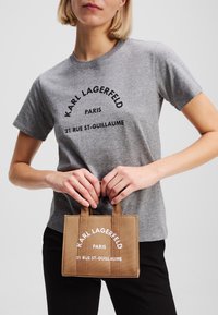 Gray short-sleeve t-shirt with black text, paired with a small brown canvas bag featuring white lettering and two top handles.
