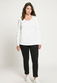 Bílá dlouhá halenka s výstřihem do V, spárovaná s černými zúženými džíny s ohrnutými nohavicemi a bílými teniskami. Jednoduchý design, měkká tkanina a klasický střih.