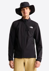 Μαύρο μπουφάν softshell με φερμουάρ, ψηλό γιακά και πλαϊνές τσέπες. Συνδυάζεται με μαύρο καπέλο με φαρδύ γείσο. Ομαλή υφή.