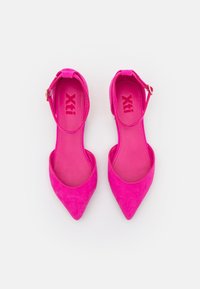 Bailarinas de ante rosa brillante con puntera afilada y correas en el tobillo con cierres de hebilla, dispuestas una al lado de la otra sobre un fondo blanco.