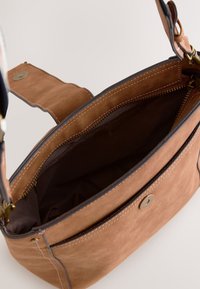 Sac bandoulière en daim marron avec rabat magnétique, fermeture éclair sur le dessus et doublure intérieure visible sur fond neutre.