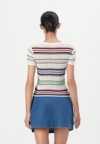 Gestreiftes Strickoberteil in Weiß mit mehrfarbigen Streifen; kurze Ärmel, eng anliegende Silhouette, gerippte Textur, kombiniert mit einem Jeansrock.
