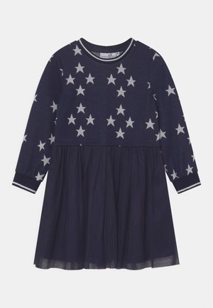 Tmavě modré dívčí šaty s dlouhým rukávem, na vrchní části s bílým vzorem hvězd a s vrstvenou tylovou sukní na spodní části.