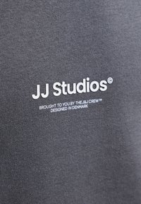 Tissu foncé avec texte blanc indiquant JJ Studios, présenté par l'équipe J&J, conçu au Danemark.