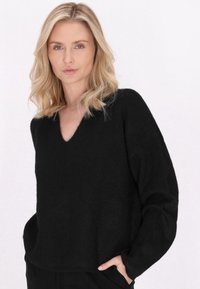 Maglione nero a maglia con scollo a V, vestibilità ampia e maniche lunghe. Morbida consistenza e dettagli con tasche laterali. Colore uniforme senza motivi.