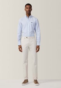Lichtblauw en wit gestreept button-down shirt, crèmekleurige chinos en bruine sneakers. Bevat een klein logo op de borst van het shirt en opgerolde mouwen.