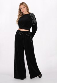 Zwarte fluwelen set met een croptop met lange mouwen en studaccenten, en wijde broek met zakken en een trekkoord in de taille.