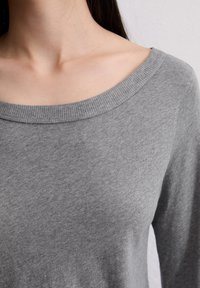 Szary sweter z długim rękawem, z szerokim, ściąganym dekoltem i miękką fakturą materiału, cechujący się luźnym fasonem i minimalną ilością szwów.
