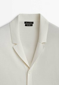 Polo à manches longues en maille couleur crème avec col, patte boutonnée et étiquette "Massimo Dutti" à l'intérieur de l'encolure.