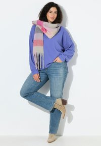 Suéter morado oversize, jeans azul claro, botas de tobillo beige y una bufanda de rayas multicolores con detalles de flecos.