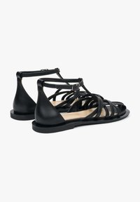 Zwarte leren sandalen met een strappy ontwerp, open neus en een platte zool. Verstelbare enkelsluiting met gespsluiting voor een veilige pasvorm.