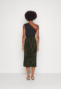 Černý top s jedním ramínkem, kombinovaný s sukní po kolena v tmavě zelené barvě s maskáčovým vzorem, hladkou texturou a sandály na kotníkovém pásku.