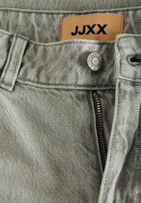 Pantalones de mezclilla gris con una tela texturizada, que presentan una etiqueta JJXX, botón de metal y cremallera para el cierre.