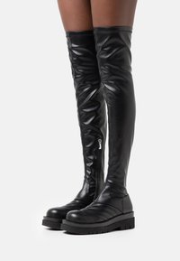 Bottes hautes noires en cuir, dépassant le genou, dotées d'une fermeture éclair latérale, de détails matelassés sur l'avant du pied et d'une semelle épaisse avec une bande de roulement bien marquée.