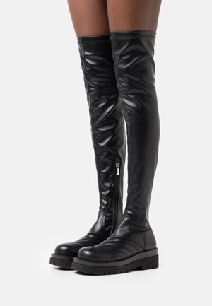 Bottes hautes noires en cuir, dépassant le genou, dotées d'une fermeture éclair latérale, de détails matelassés sur l'avant du pied et d'une semelle épaisse avec une bande de roulement bien marquée.