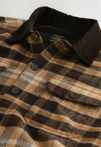 Brown and tan plaid shirt featuring a corduroy collar, two chest pockets, and dark buttons. Soft fabric texture with a checked pattern.