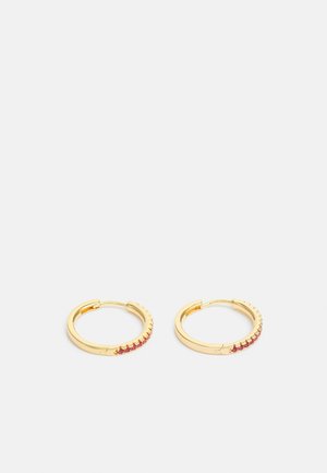 Boucles d'oreilles créoles en or avec une rangée de petites pierres précieuses rouges sur le bord extérieur, présentées sur un fond blanc uni.