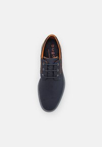 Chaussure en textile bleu marine avec un bout rond, six œillets, des accents orange, et une semelle en caoutchouc grise. Dotée d'une tige texturée pour la respirabilité.